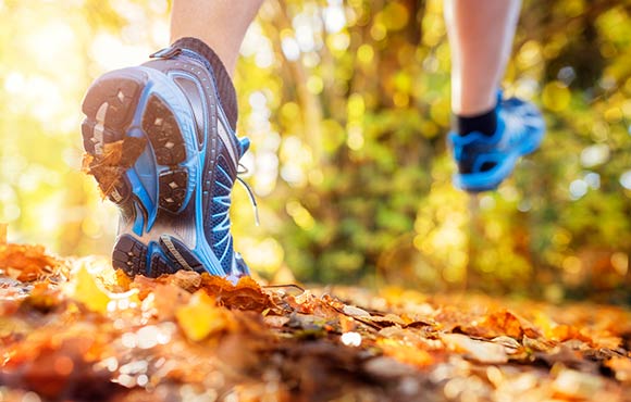 Photo of woman in blue sneakers walking through fallen leaves