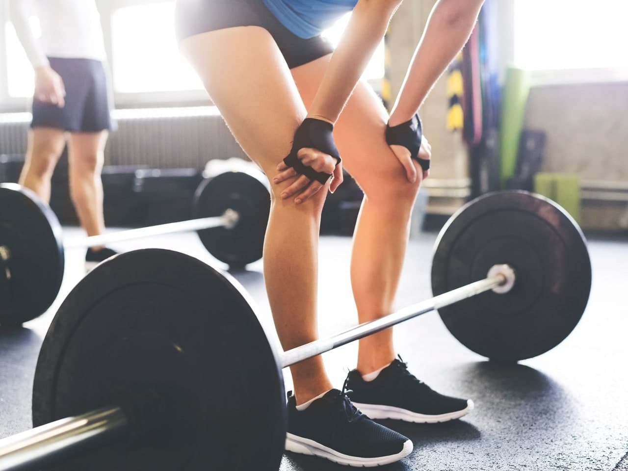 Photo of woman's legs behind barbell, she's bent down and her hands are on her knees