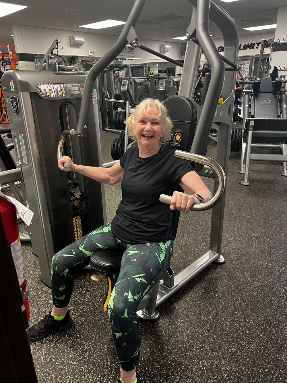 Older woman smiling while she works out at the chest press machine at AFAC gym