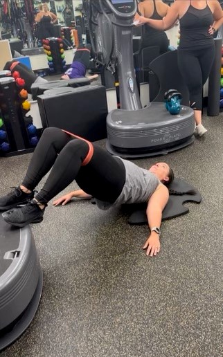 Woman laying on floor at AFAC gym with feet on a Power Plate and resistance band around her thighs