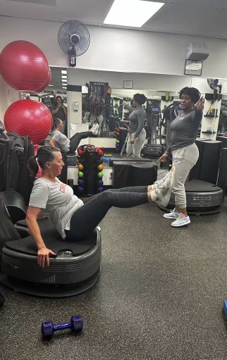 Woman exercising on Power Plate while a personal trainer looks on at AFAC gym