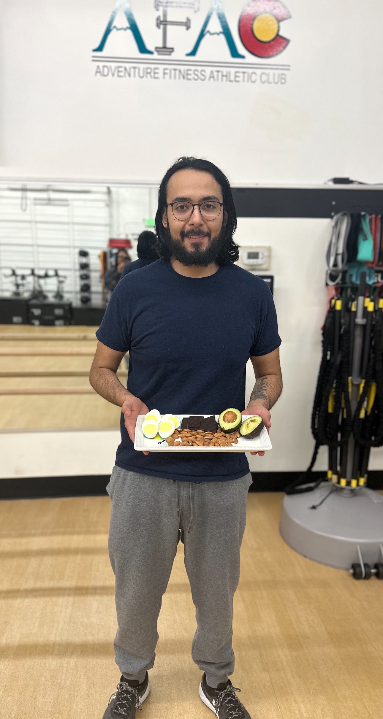 Man standing at AFAC gym, holding a plate full of food including avocados, almonds, and hard-boiled eggs