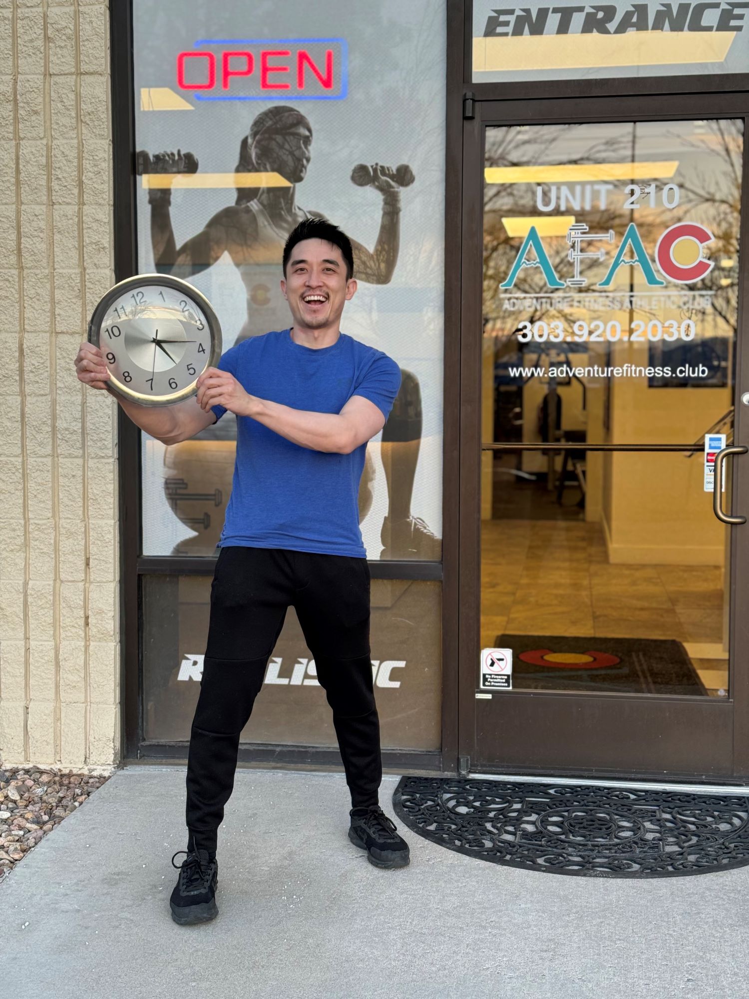 Man smiling and holding clock while standing in front of AFAC gym in Thornton CO