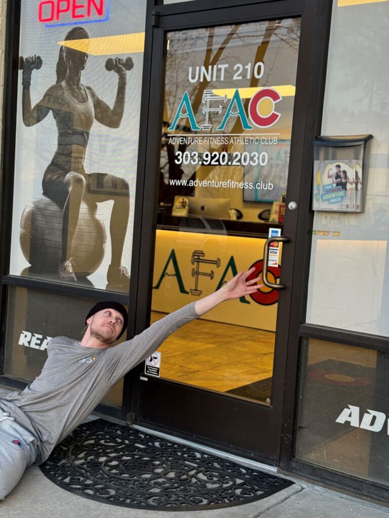 Man reclining on the ground in front of AFAC gym, reaching for the handle on the front door