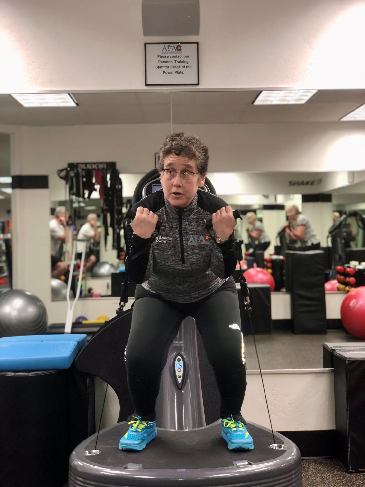 Susan Schaffner, owner of AFAC gym, squats on a Power Plate while holding small dumbbells