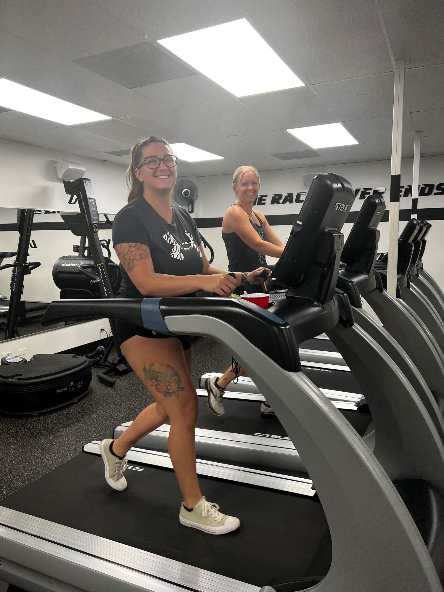 Two smiling ladies walk on treadmills at AFAC gym.