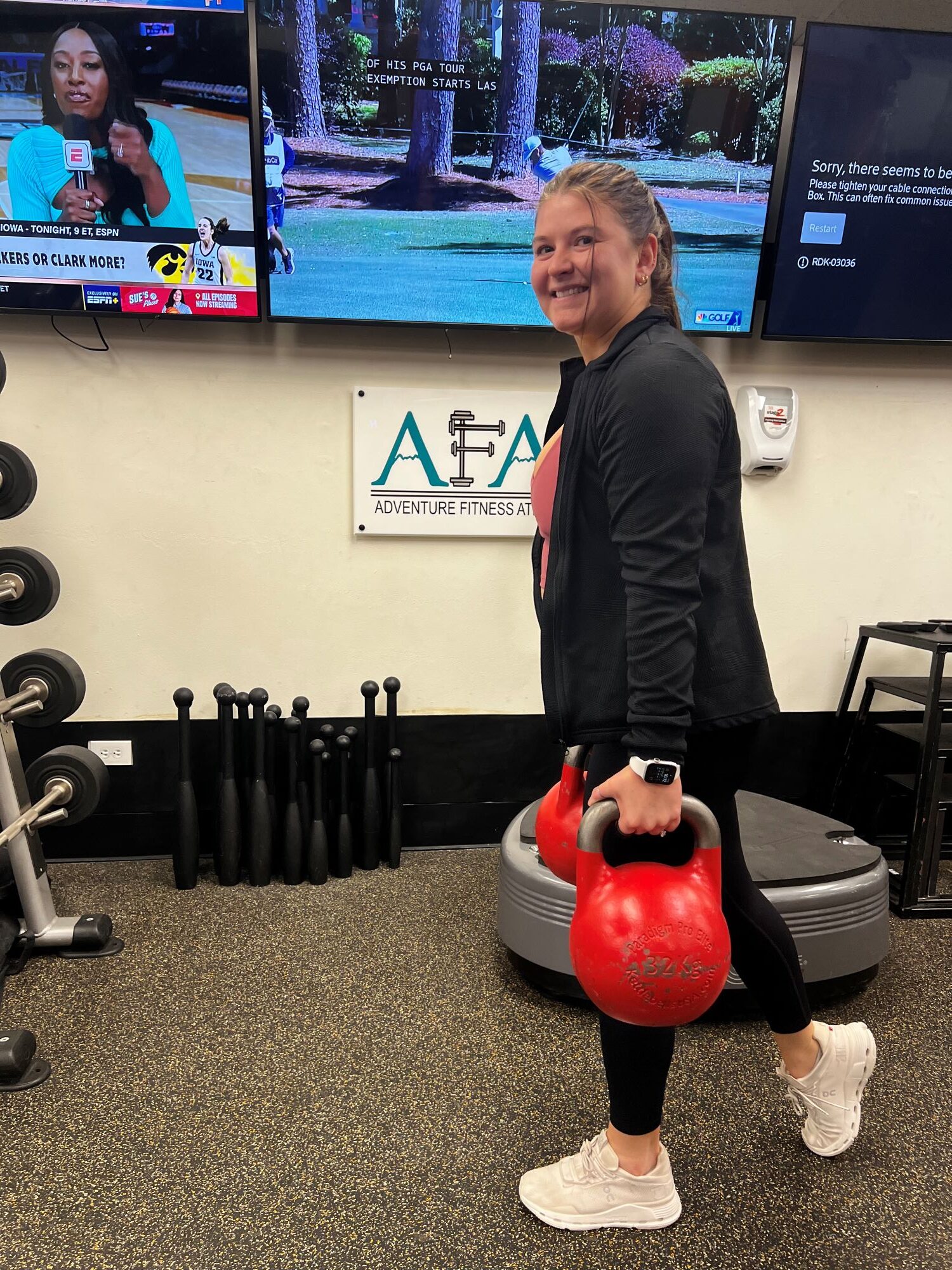 Woman at AFAC gym performs the Farmer's Carry with red kettlebells