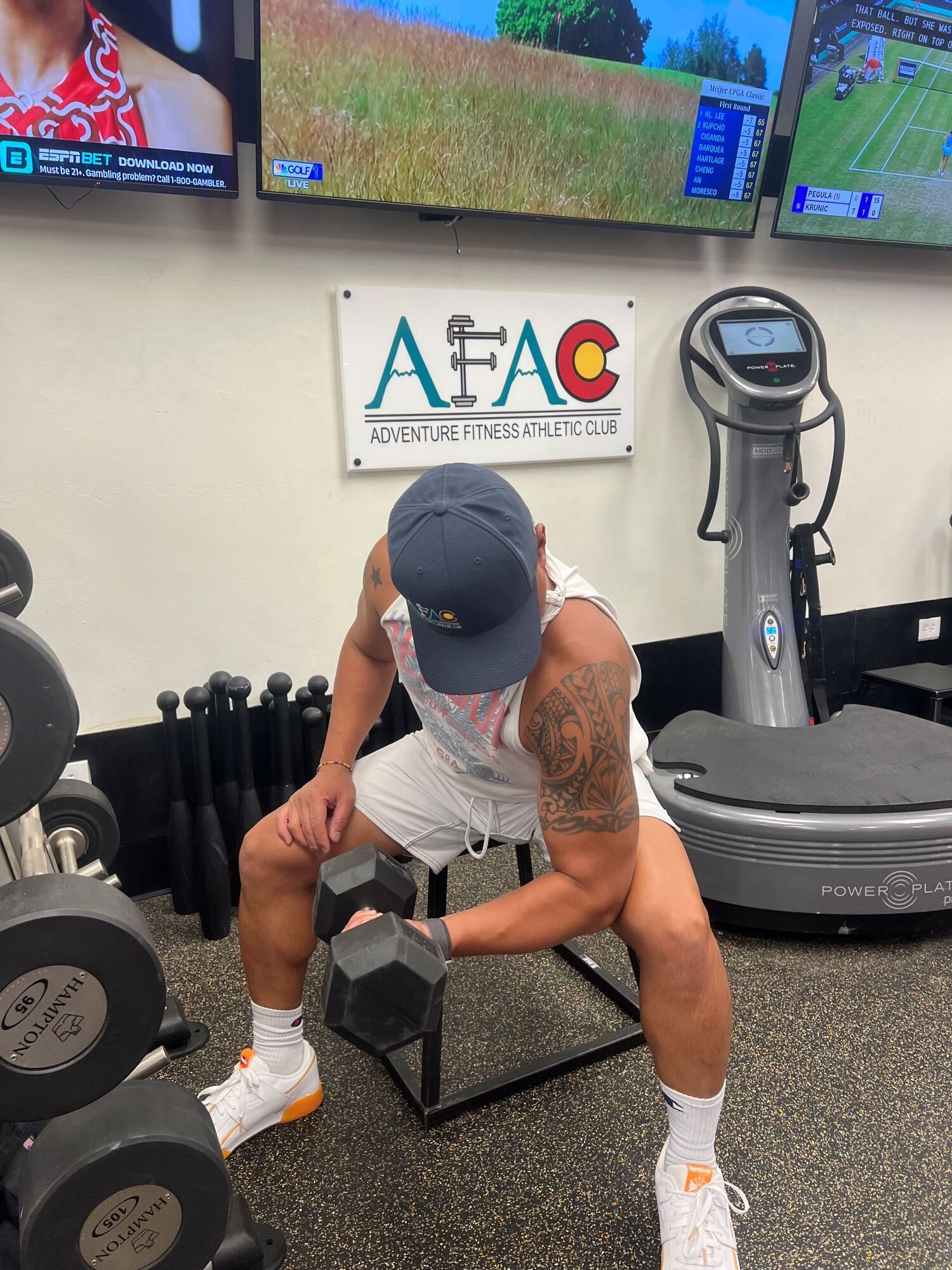 Man sitting on a bench at AFAC gym and lifting one dumbbell in his left hand