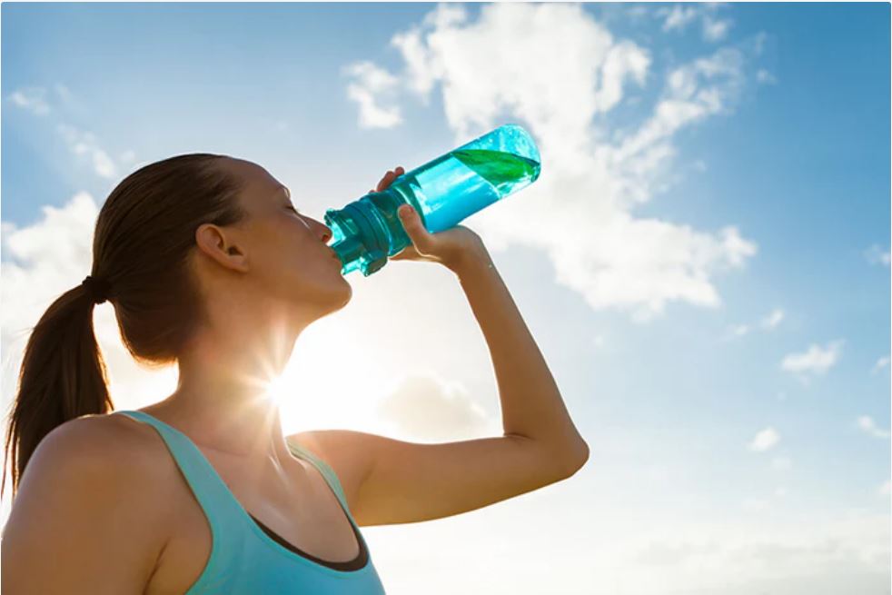 Woman outside on a sunny day drinking from a clear blue plastic bottle