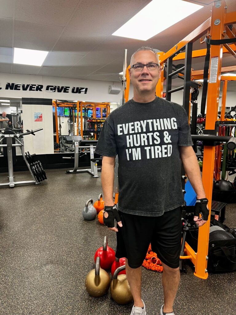 Man standing in AFAC gym wearing a black T-shirt that says, "Everything hurts and I'm tired"