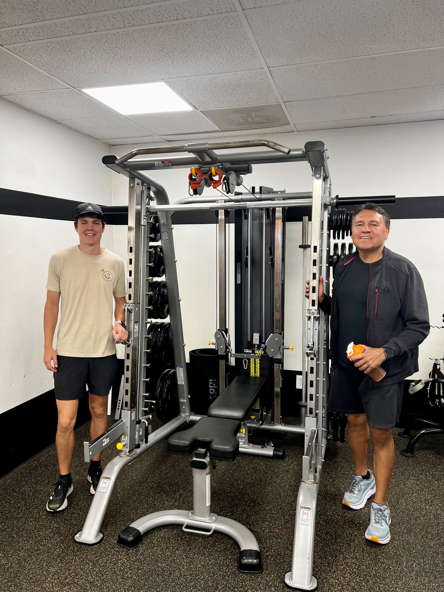 Two smiling men standing by a squat rack at AFAC gym