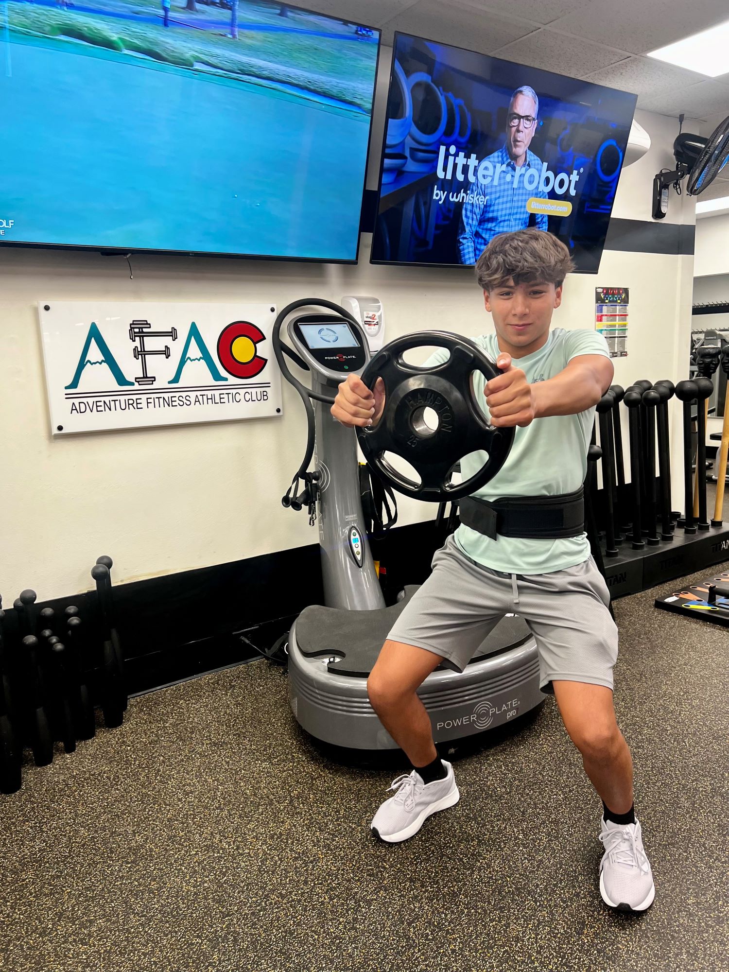 A young man holds a weight plate in front of him while performing a squat at AFAC gym