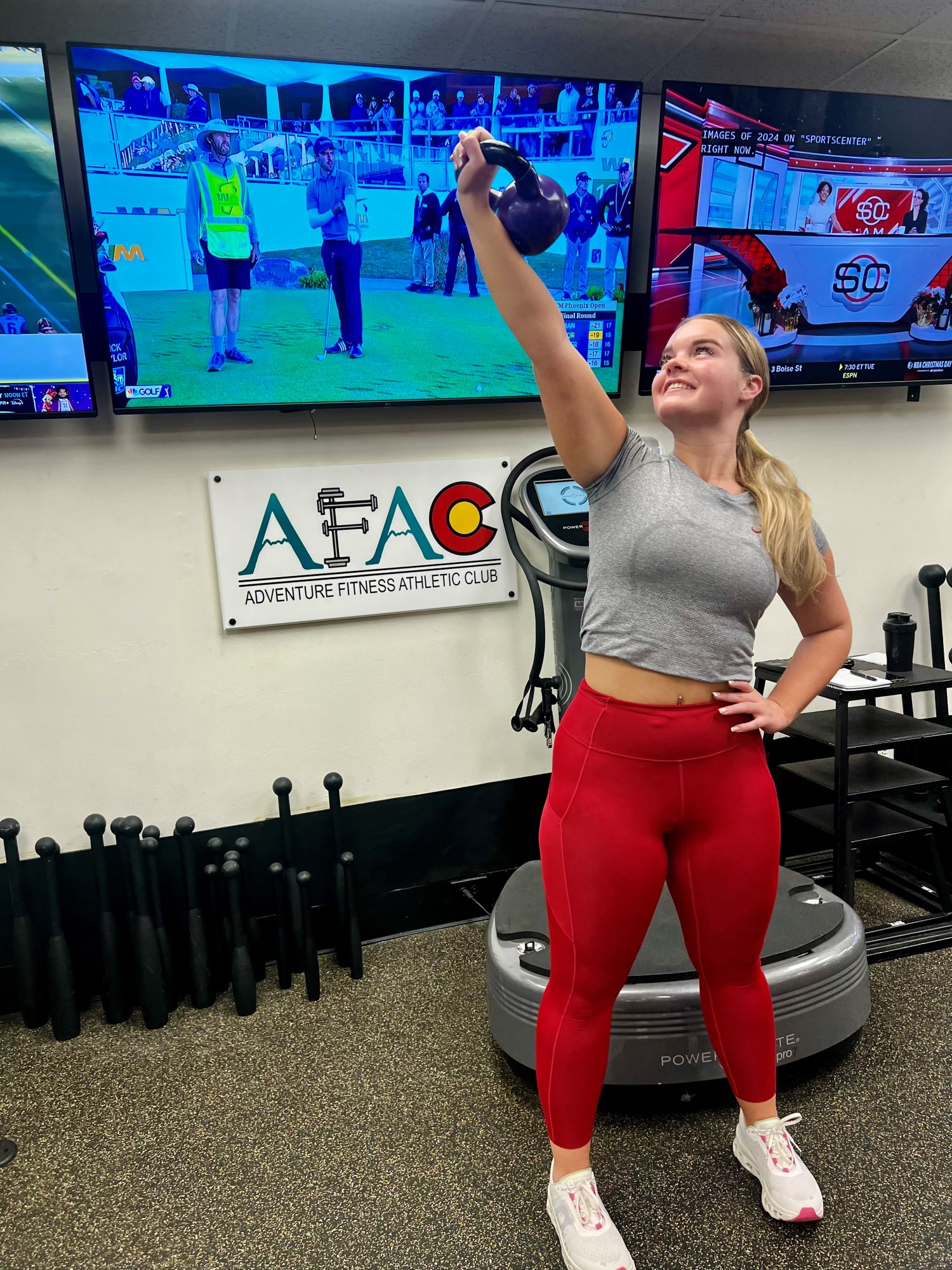 Young woman at AFAC gym holds kettlebell over her head with her right hand