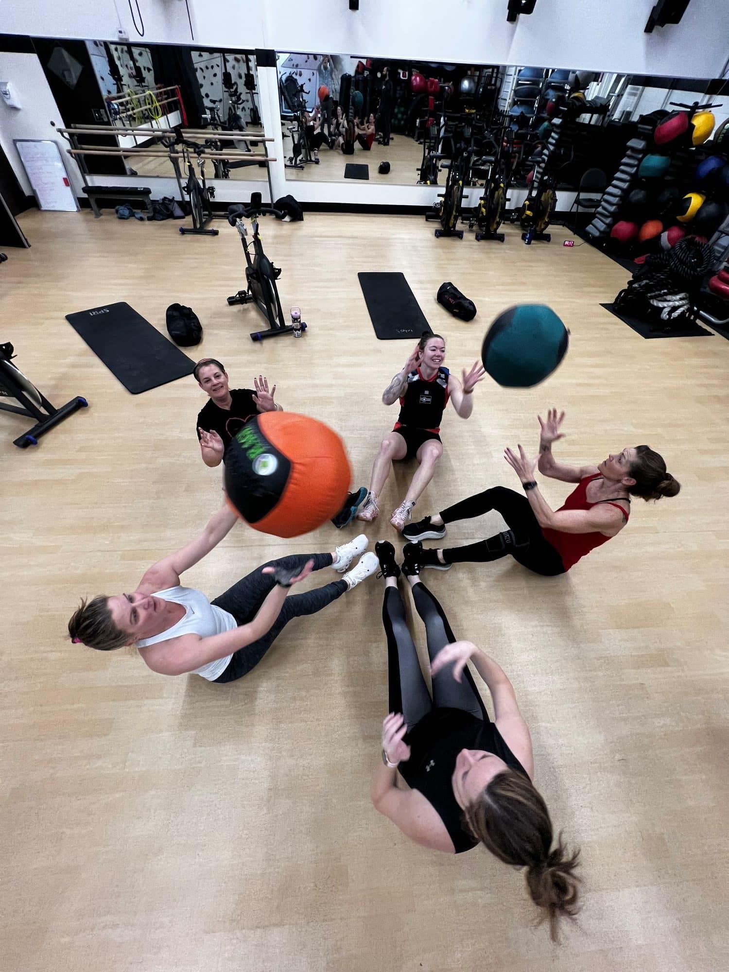 Five women sit in a circle at AFAC gym throwing exercise balls to each other