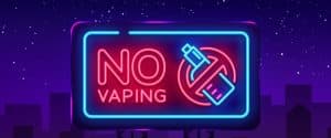 Pink and blue neon sign with purple background that says NO Vaping