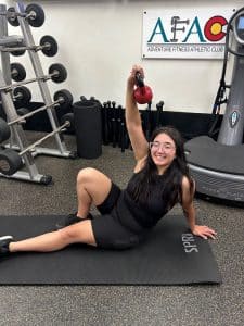 Girl sitting on mat at AFAC gym lifting a kettlebell above her head