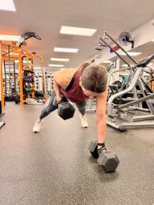 Woman at AFAC gym performs rows with dumbbells while in a plank position (also known as renegade rows)