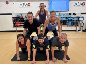 6 smiling members of AFAC gym form a human pyramid in a workout room