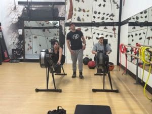 Personal trainer at AFAC gym stands behind two women working out on rowing machines