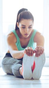 Woman sitting on gym floor holding her toes in a static stretch