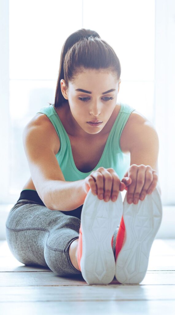 Woman sitting on gym floor holding her toes in a static stretch