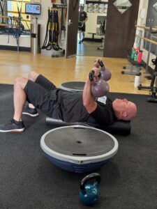 Man at AFAC gym laying on gym floor lifting kettlebells above his body