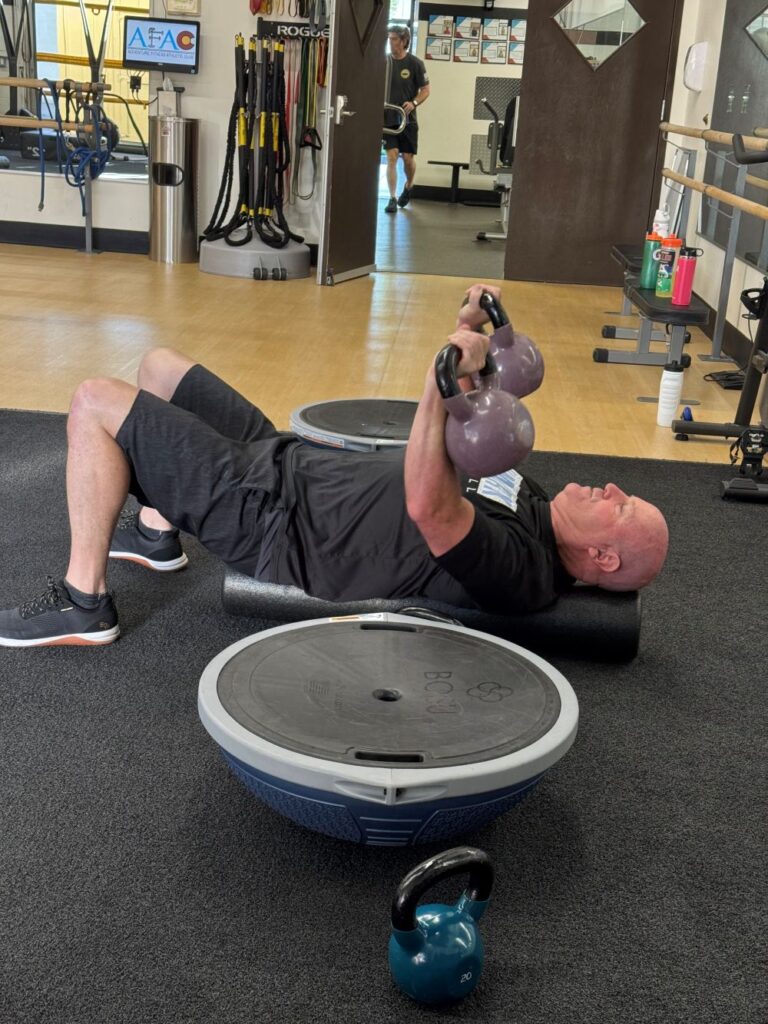 Functional Fitness Workouts at the Gym Man at AFAC gym laying on gym floor lifting kettlebells above his body