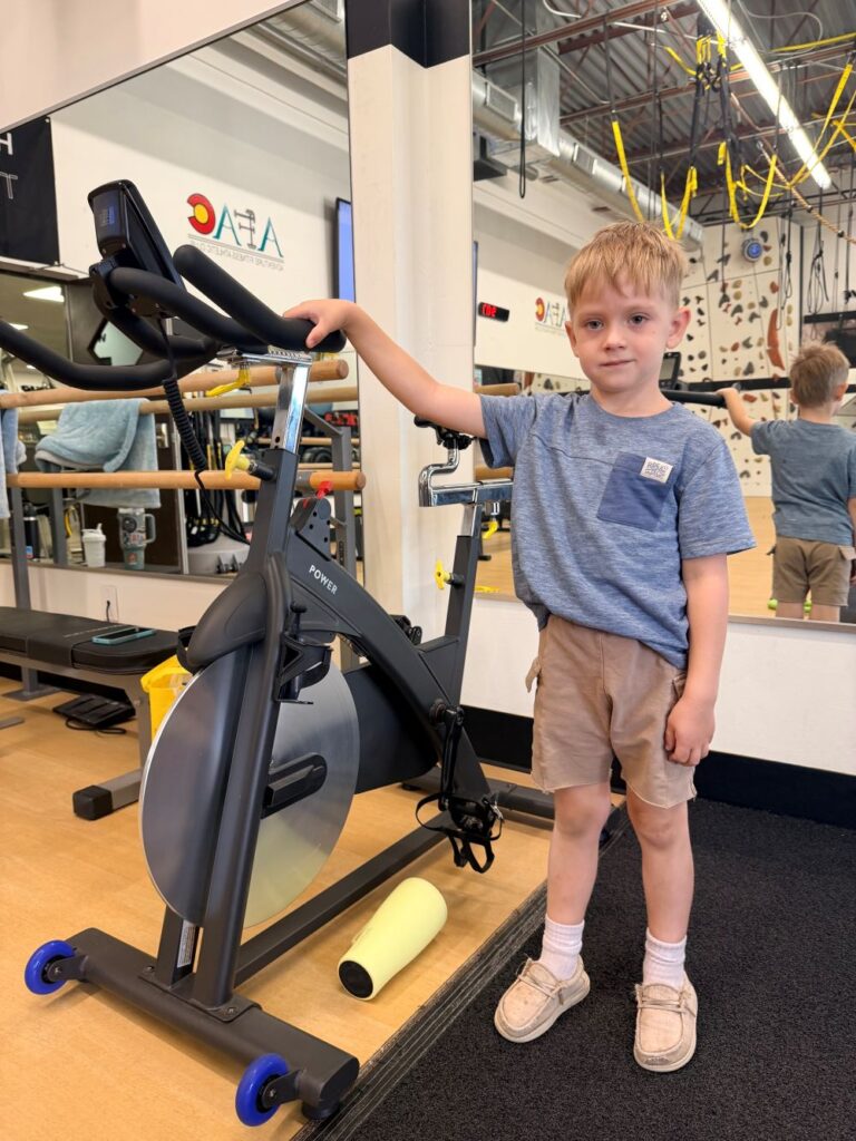 Young boy stands next to spin bike at AFAC gym