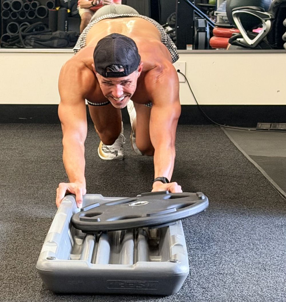 Man pushes sled weight across the turf area at AFAC gym.