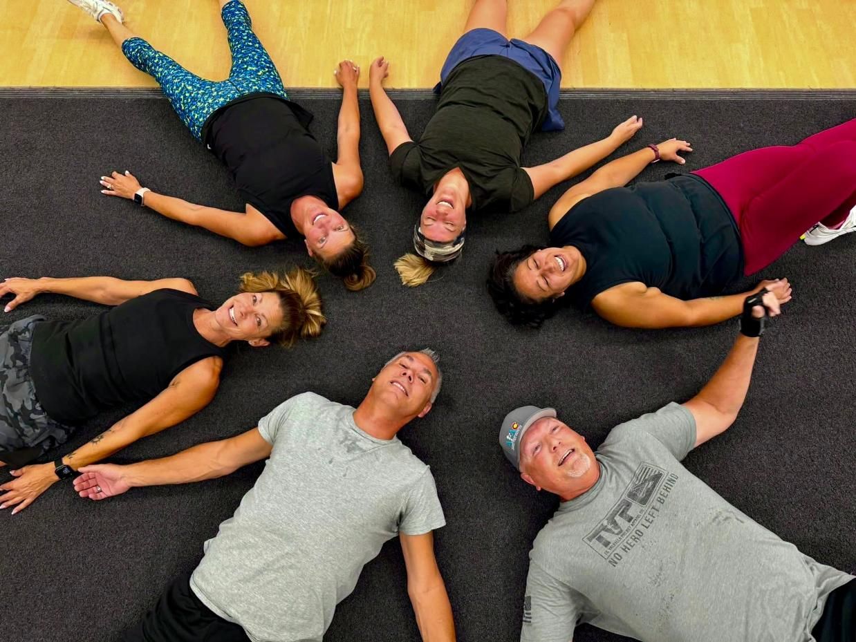 Two male and four female AFAC gym members laying on the floor in a circle and smiling