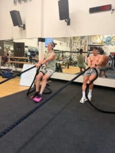 Two men pull sleds across the turf area of AFAC gym