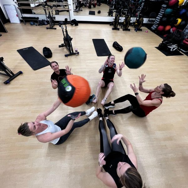 Five women sit in a circle at AFAC gym throwing exercise balls to each other